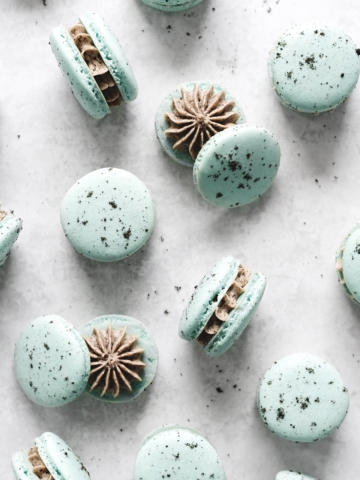 Blue macarons showing oreo filling inside scattered on gray background
