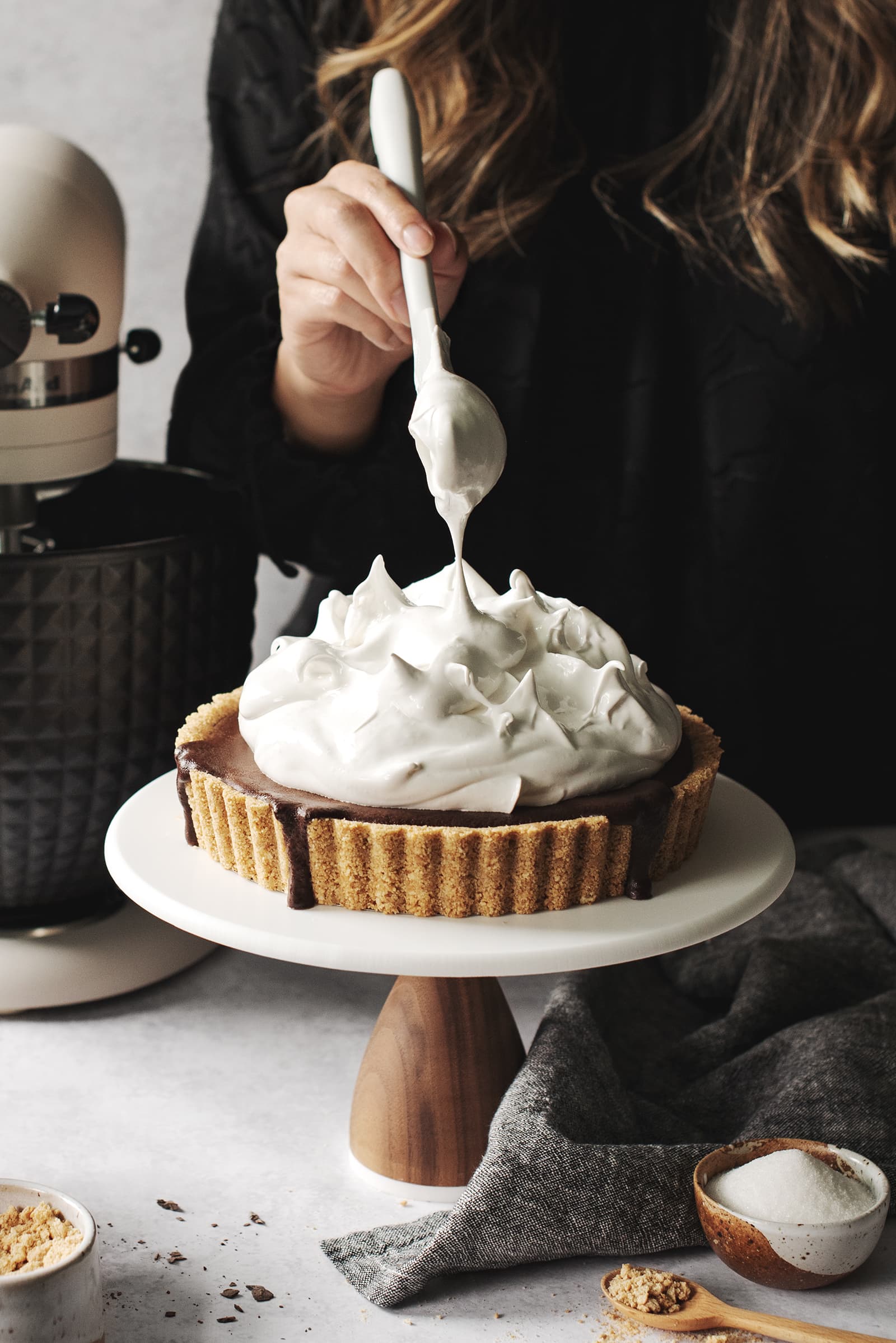 Girl pulling a spatula away from a mount of meringue on top of tart