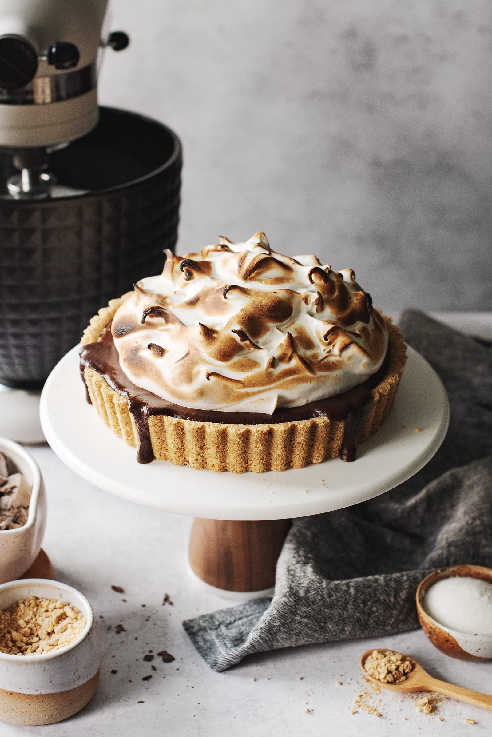 Sโmores tart with toasted meringue on a cake stand.