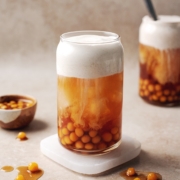 Glass of sweet potato bubble tea with sweet potato boba pearls and a layer of sweet cream dripping into black tea