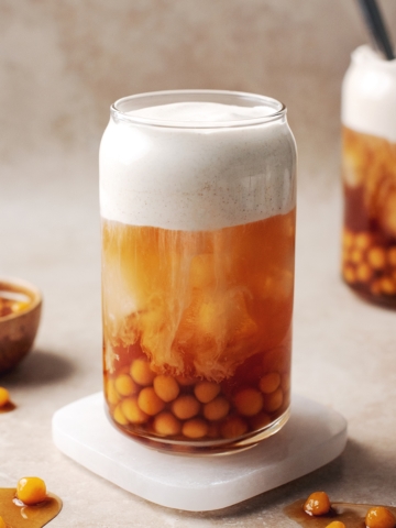 Glass of sweet potato bubble tea with sweet potato boba pearls and a layer of sweet cream dripping into black tea