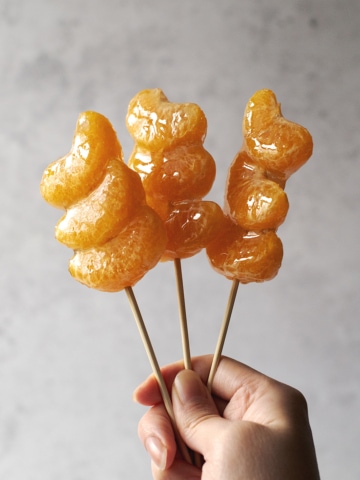 Hand holding skewers of tangerine tanghulu