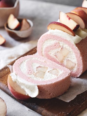 A slice of white peach swiss roll cake cut from the roll