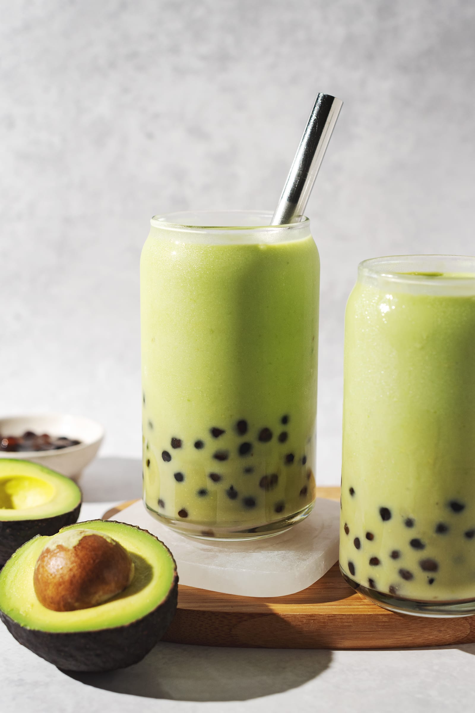 Two glasses of avocado bubble tea on a wooden platter.