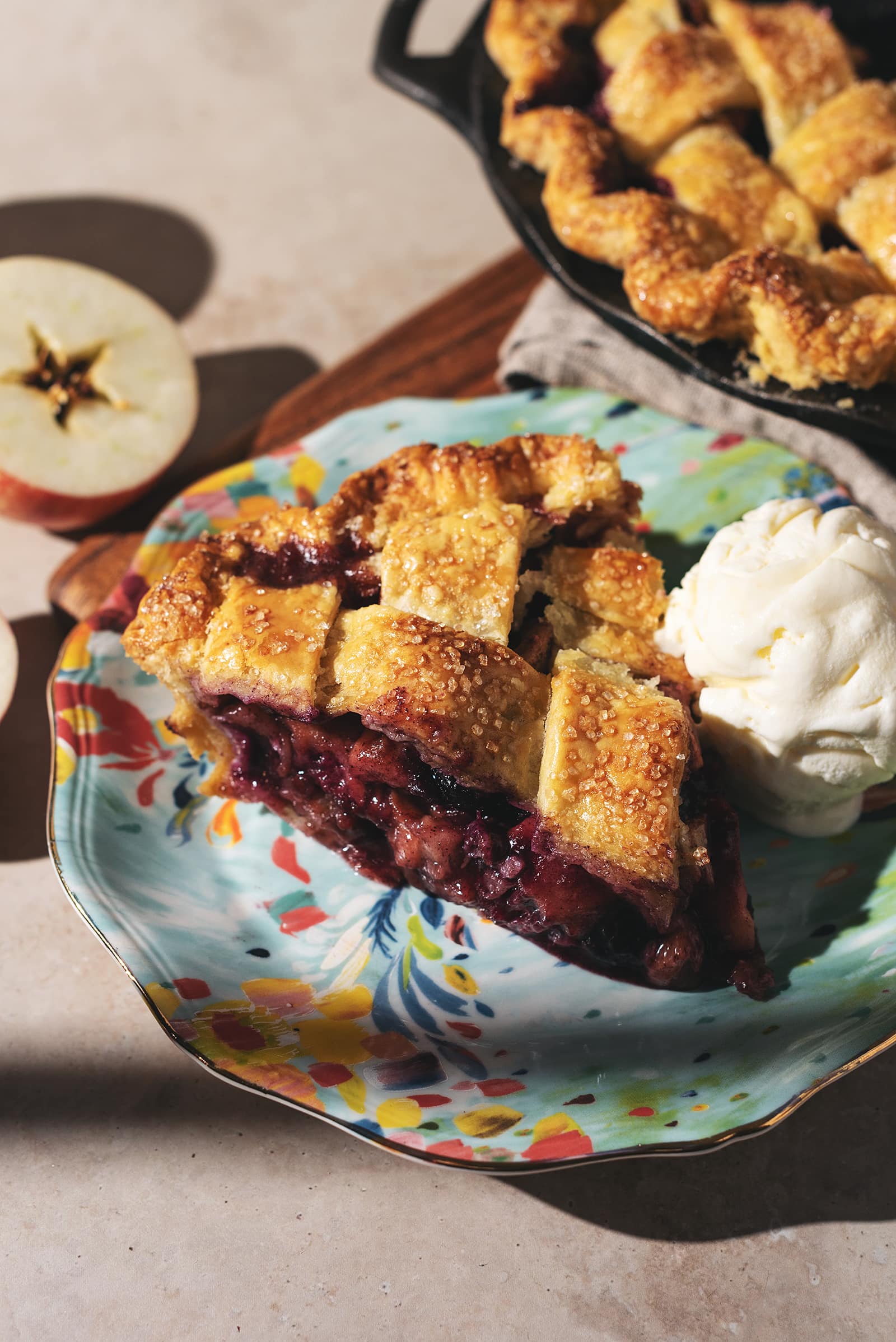 A slice of blueberry apple pie on a plate with a scoop of vanilla ice cream.