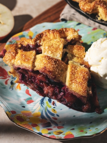 A slice of blueberry apple pie on a plate with a scoop of vanilla ice cream.