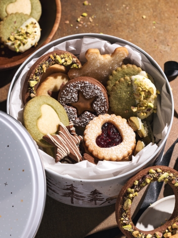 Assorted butter cookies in a round tin with cookies scattered around it.