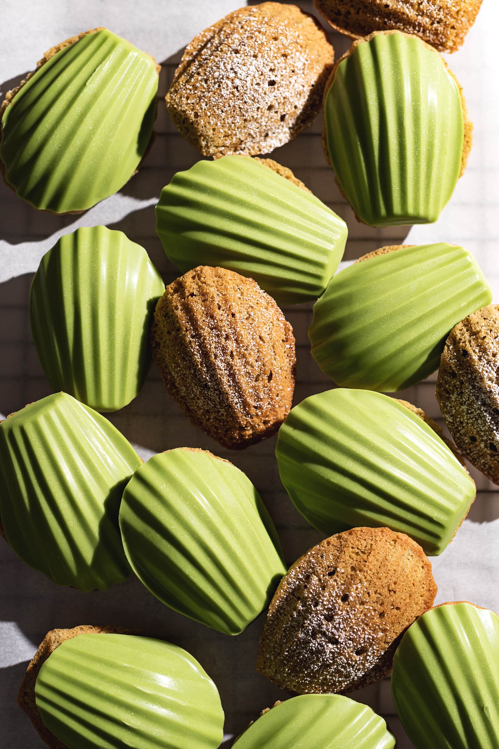 Matcha madeleines scattered on parchment paper, some plain and some with a matcha chocolate shell.