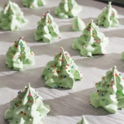 Meringue christmas trees covered in rainbow sprinkles on a baking sheet.