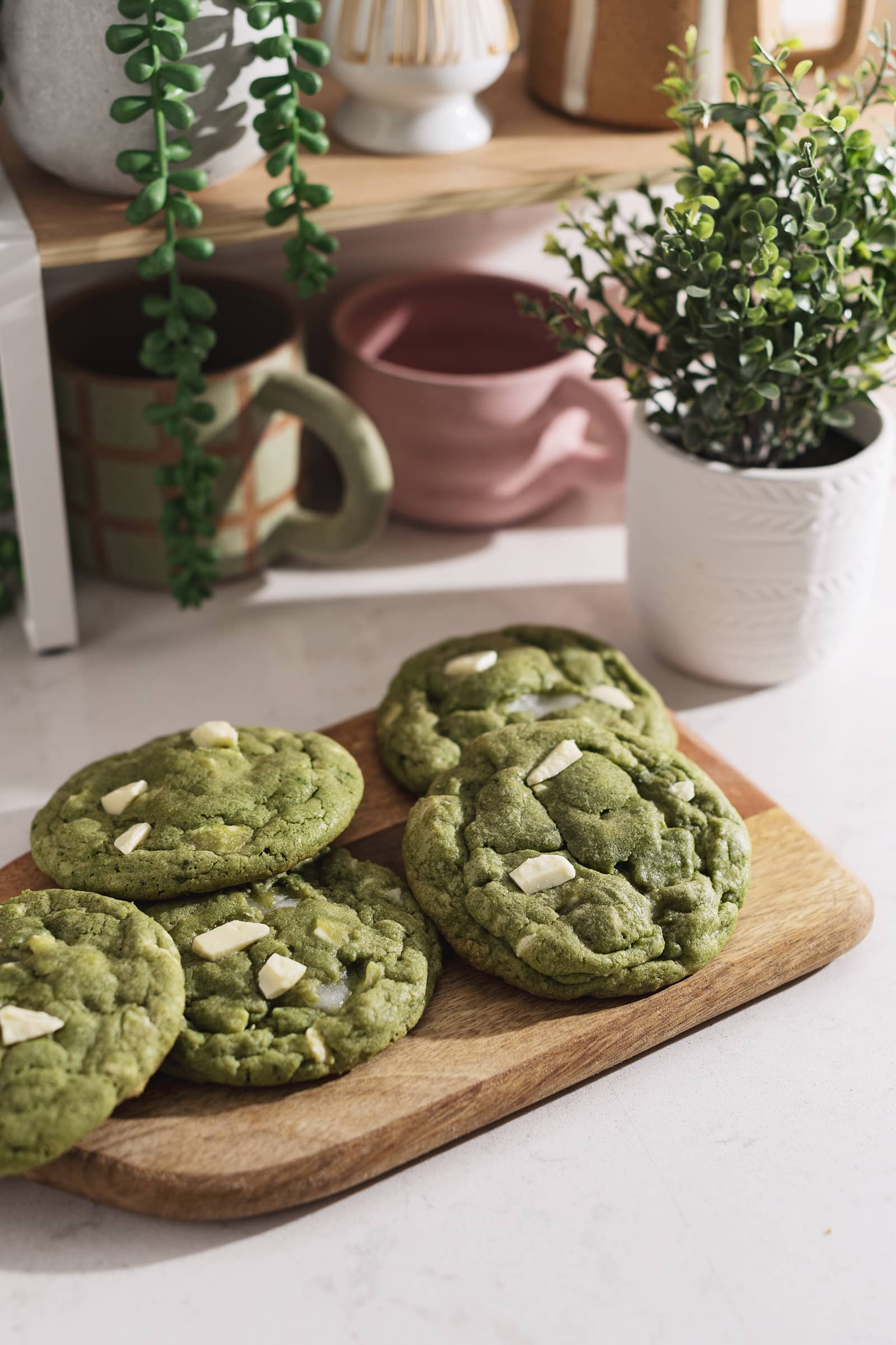 Matcha mochi cookies on a wooden board in front of a shelf.