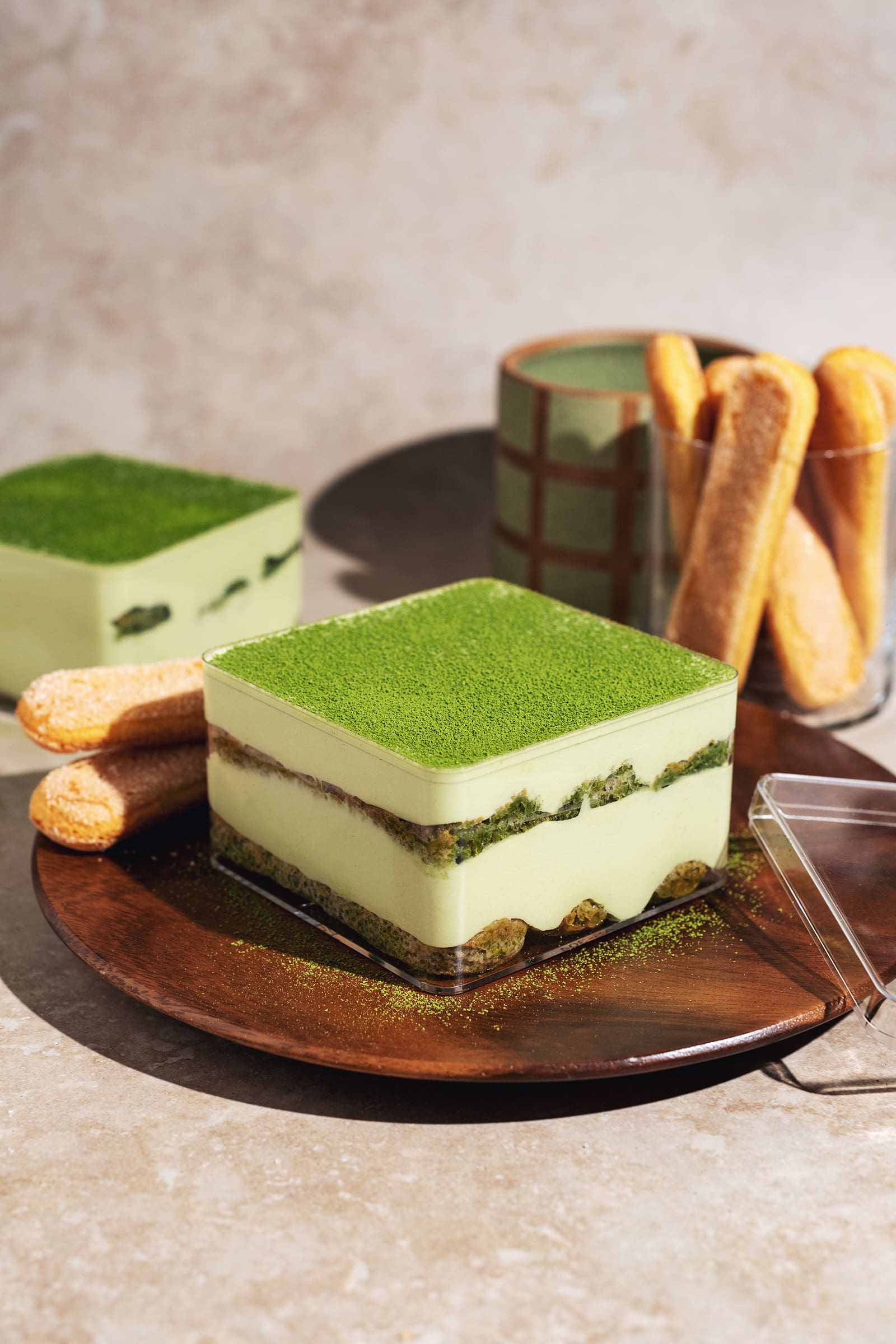 Matcha tiramisu layers in a clear box on a wooden plate.