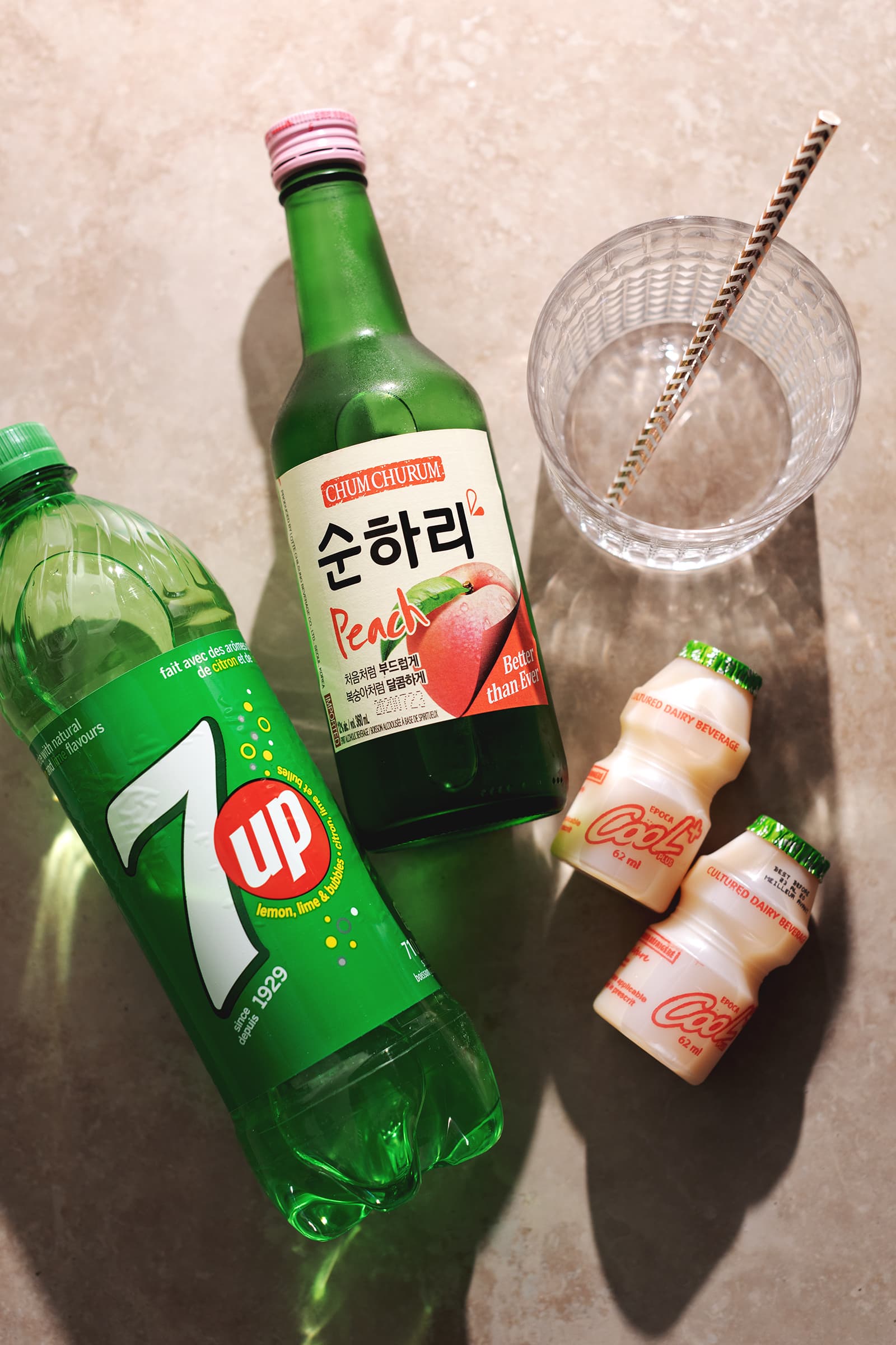 Bottles of 7-Up, Soju, and Yakult laying on table.