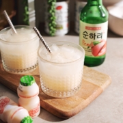 Soju yakult cocktail in a glass with soju bottle in the background and yakult in the foreground.