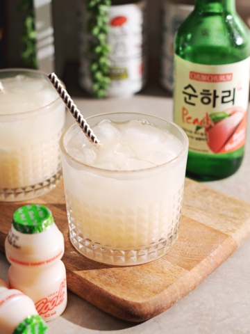 Soju yakult cocktail in a glass with soju bottle in the background and yakult in the foreground.