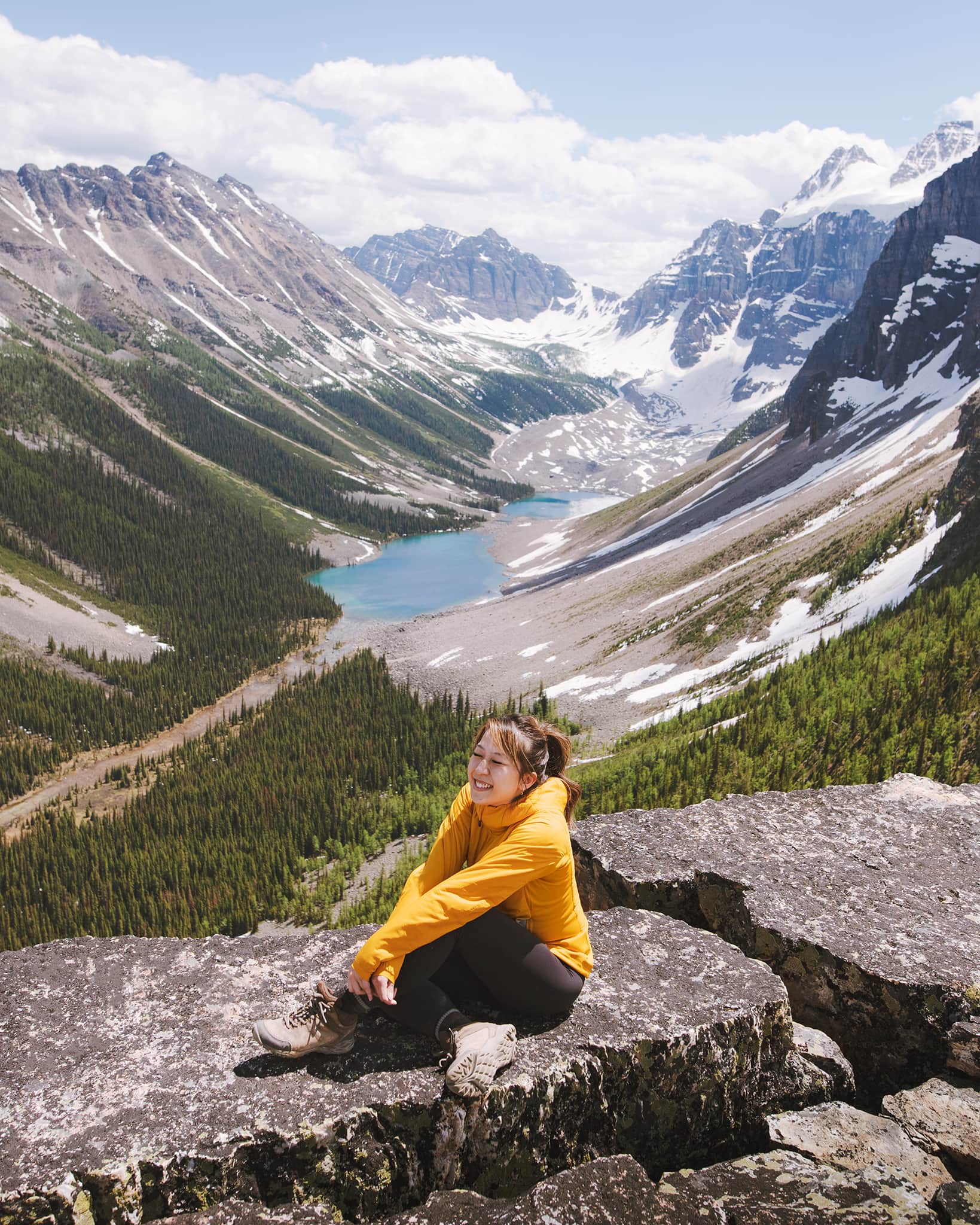Girl in yellow jacket sitting in front of mountain and lake view.
