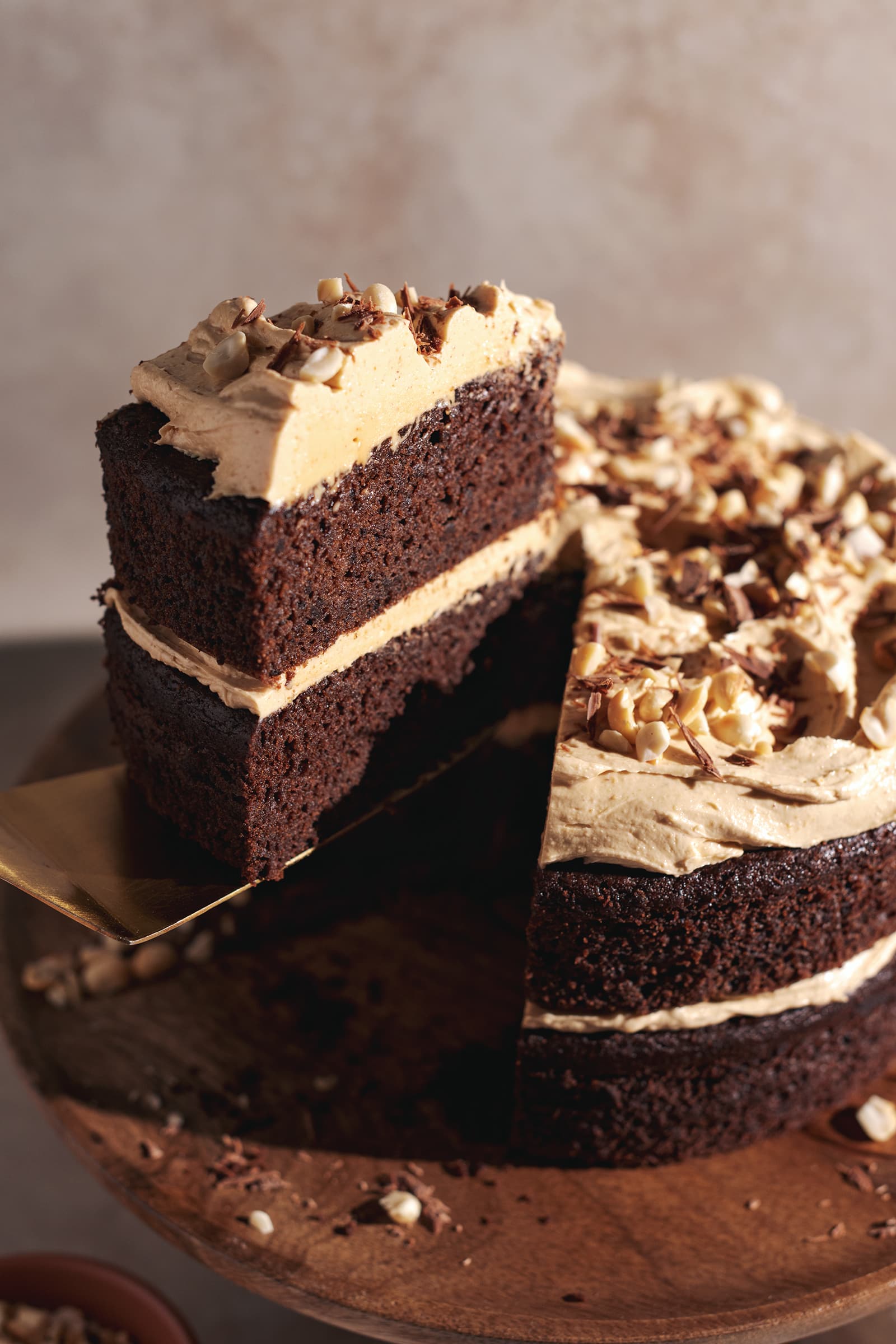 A cake slice being lifted up from the rest of the cake with a gold cake server.