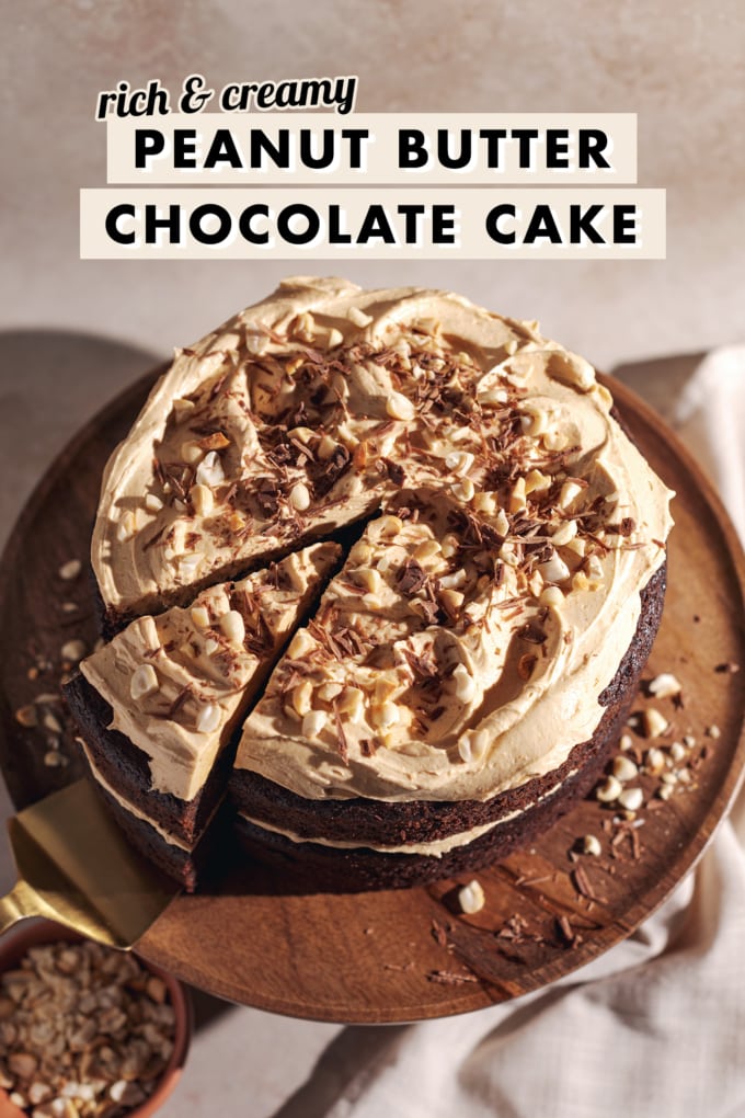 A slice cut out of a peanut butter chocolate cake on a wooden cake stand.