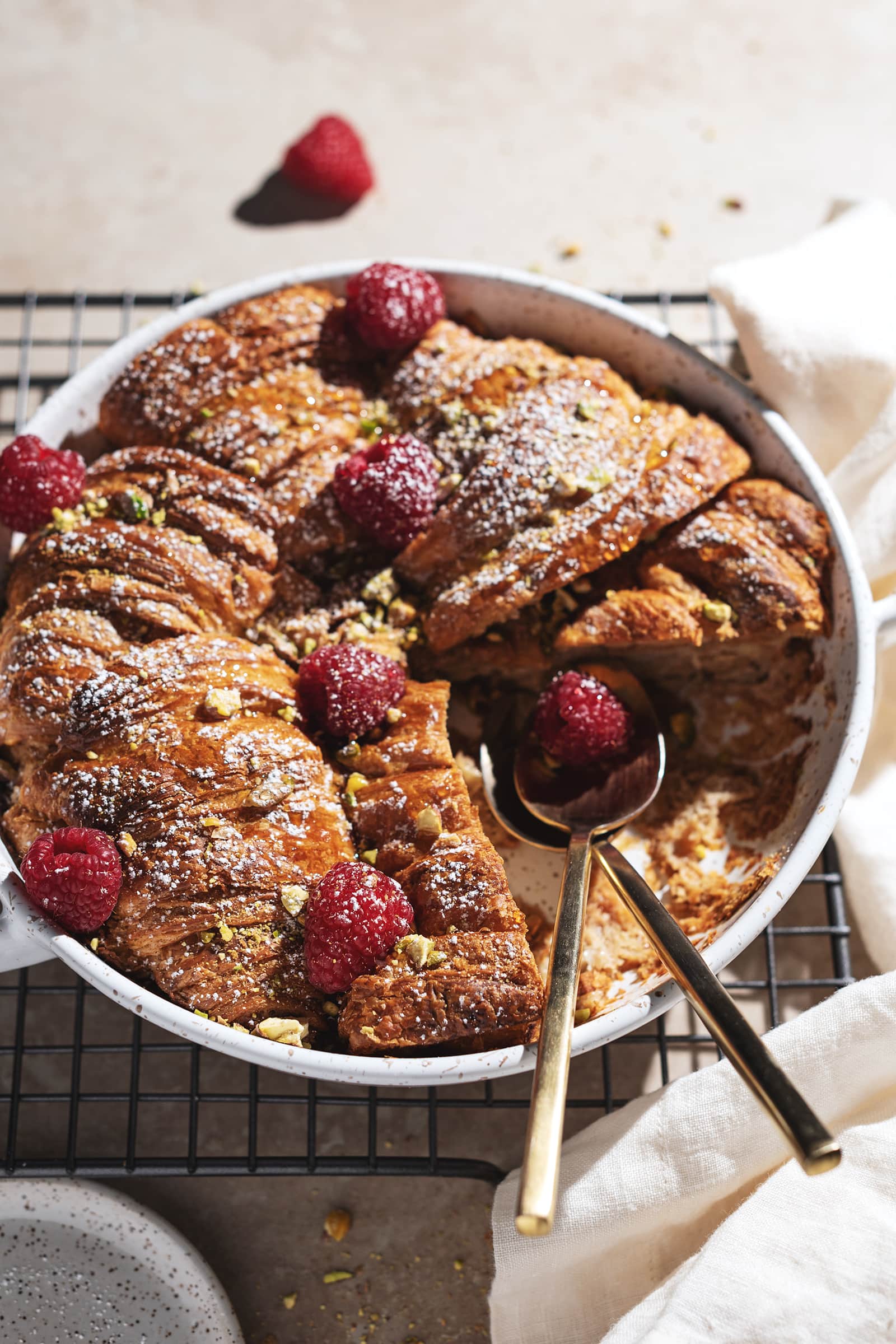 Croissant bread pudding in a baking dish with two spoons where a slice was cut out from it.