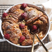 Croissant bread pudding in a baking dish with two spoons where a slice was cut out from it.