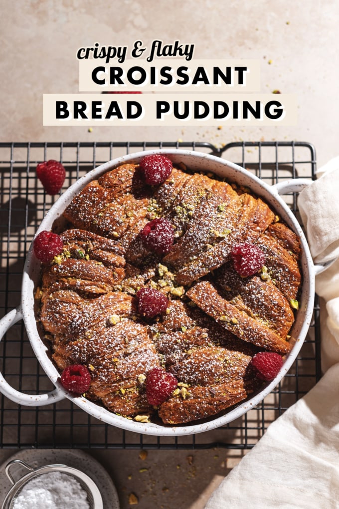 Baking dish filled with croissants sprinkled with raspberries, pistachios, and powdered sugar.