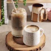 A glass of iced hojicha latte and a mug of hot hojicha latte sitting on wood platter.