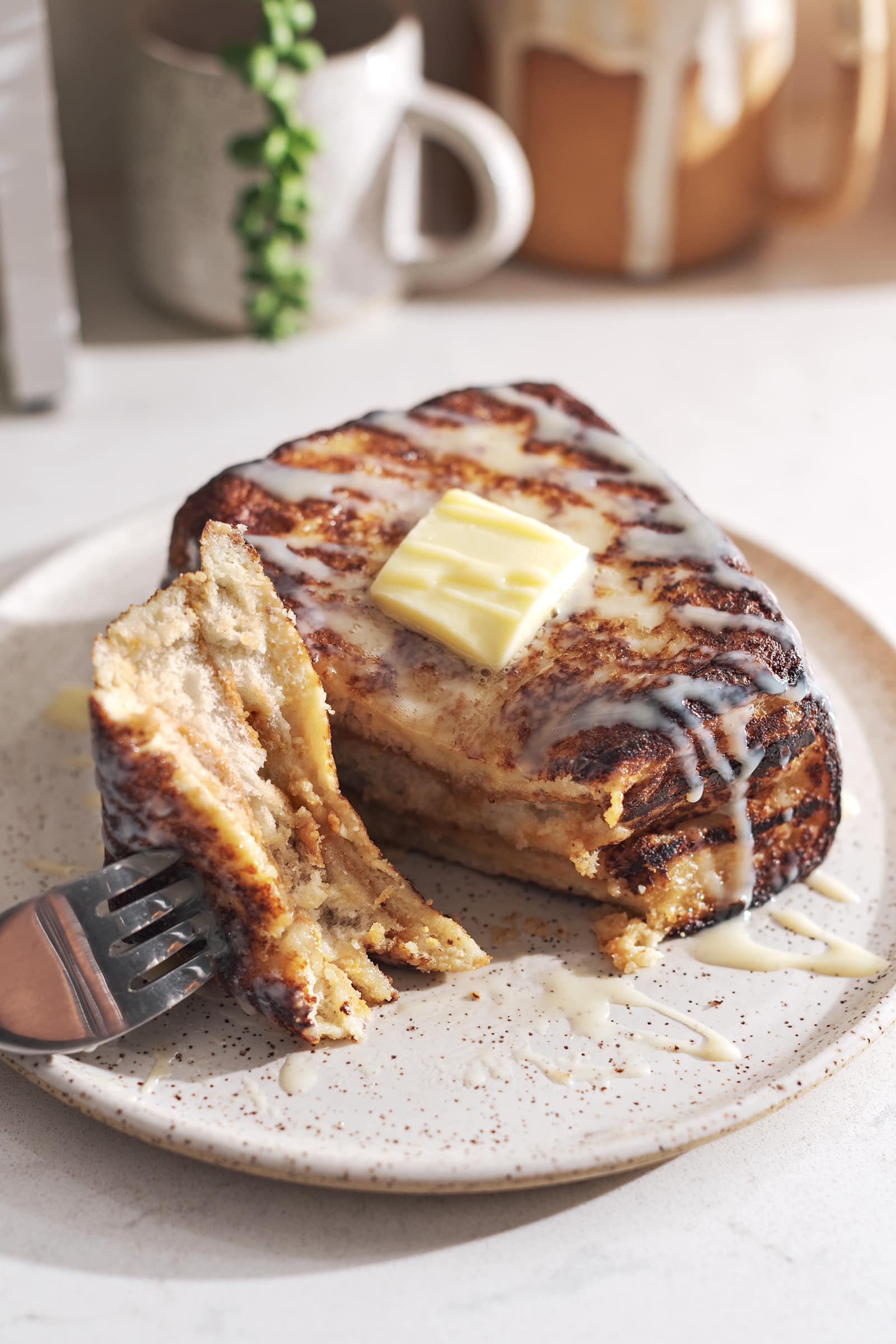 Fork with a piece of french toast resting on a plate next to the rest of the toast.
