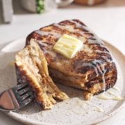 Fork with a piece of french toast resting on a plate next to the rest of the toast.