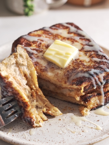 Fork with a piece of french toast resting on a plate next to the rest of the toast.