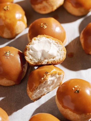 Salted caramel profiterole cut in half to show whipped cream filling inside.
