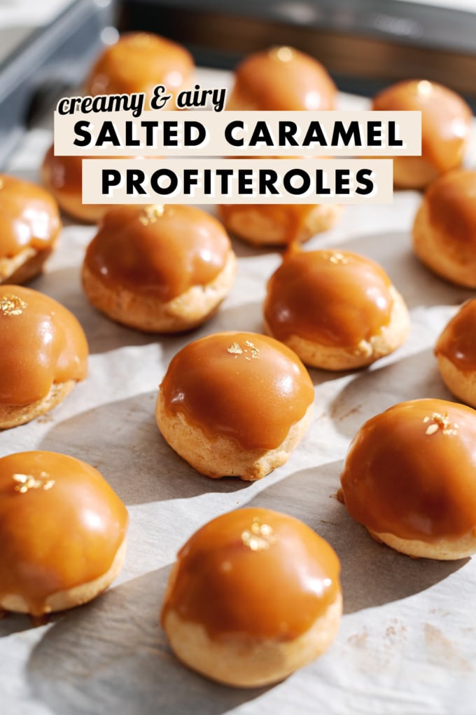Profiteroles covered with salted caramel and gold flakes lined up parchment paper.