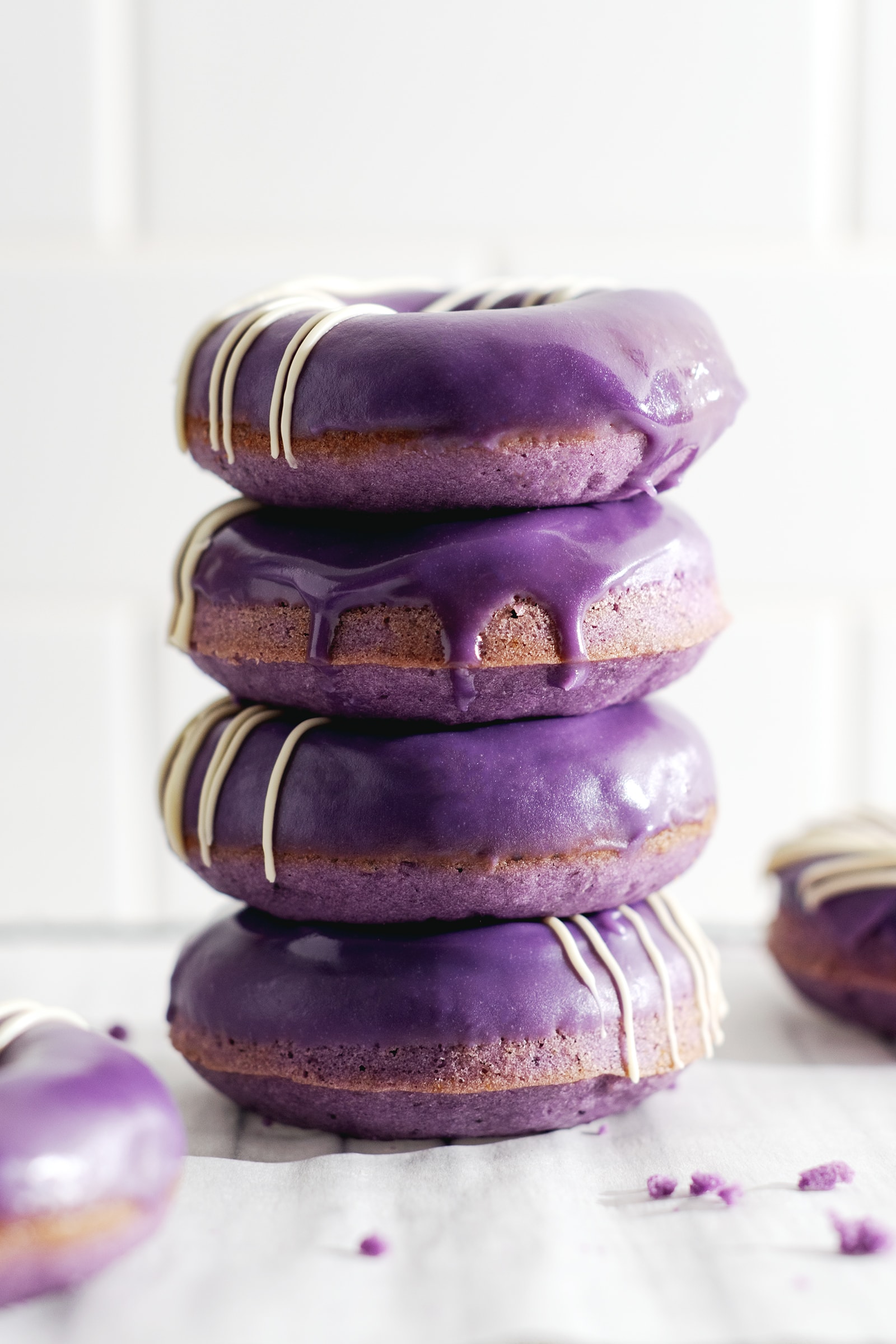 Four ube donuts stacked on top of each other with glaze dripping down the front.