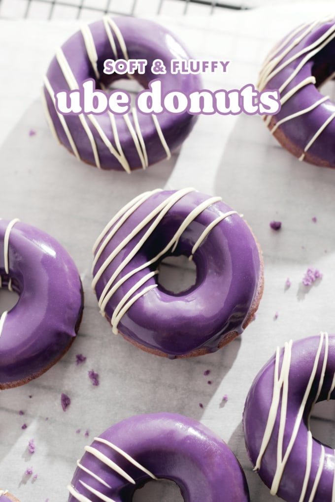 Purple ube donuts with white chocolate drizzles scattered on parchment paper.