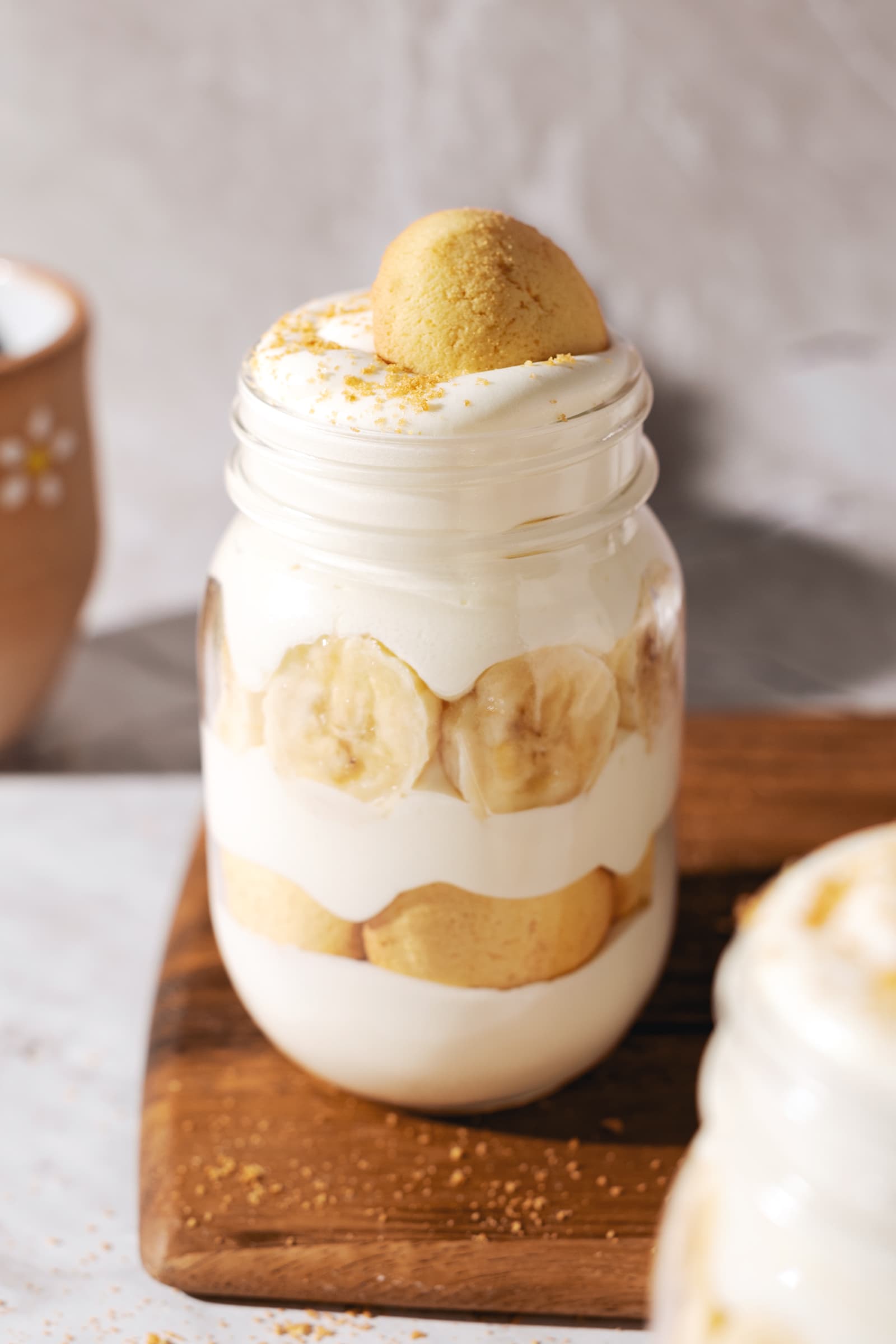 A jar of layered banana pudding on wooden board.