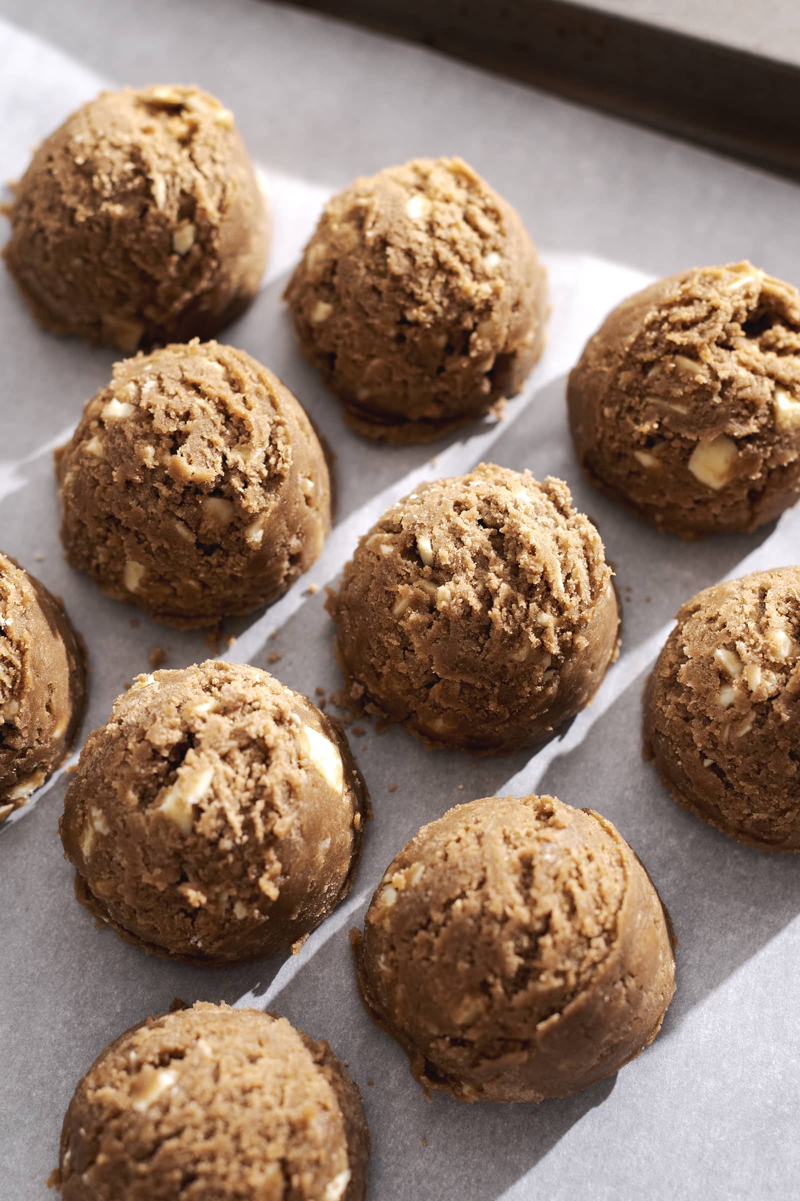 Balls of unbaked cookie dough lined up on parchment paper.