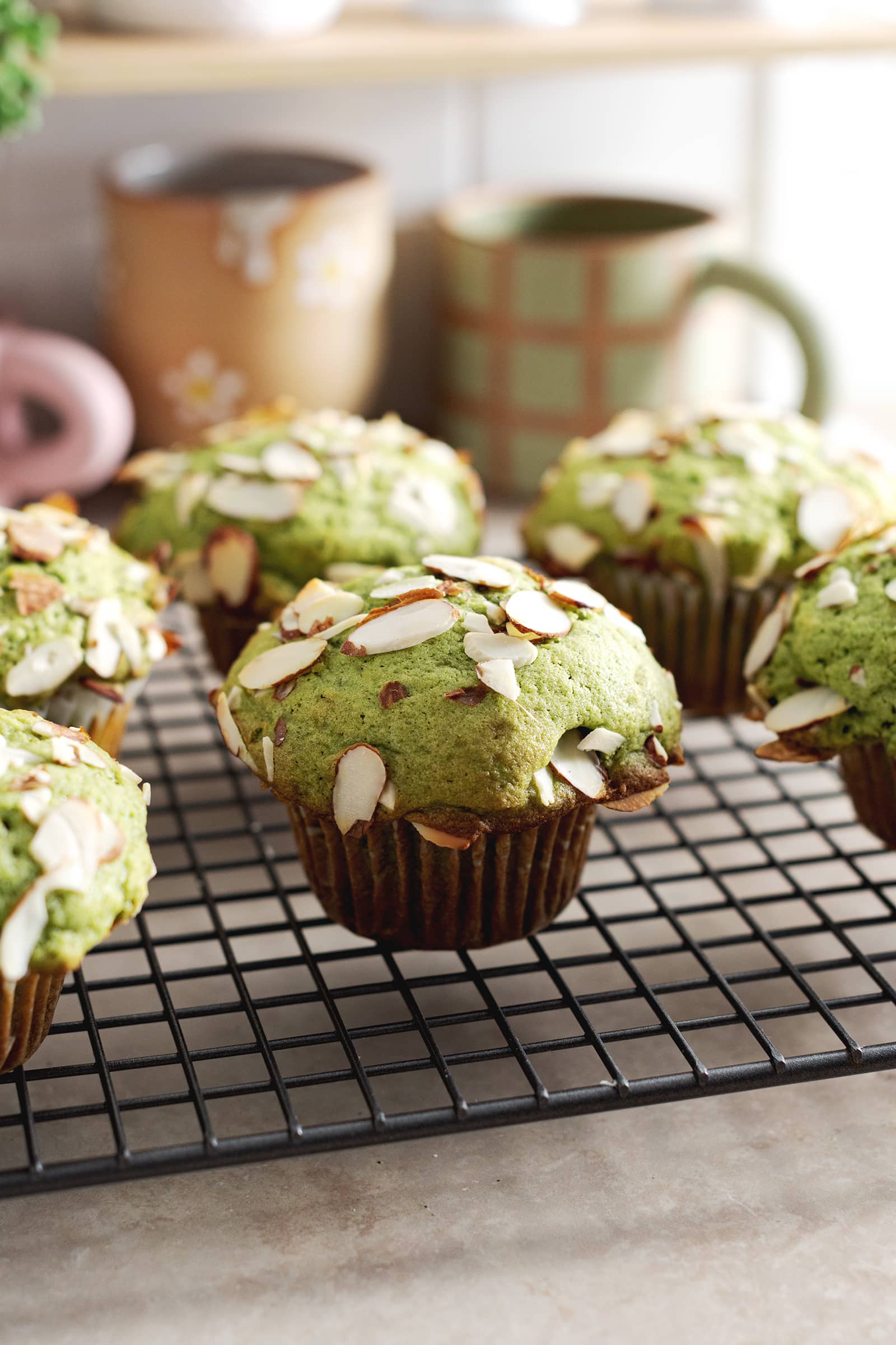 Matcha muffins topped with sliced almonds sitting on a wire rack.