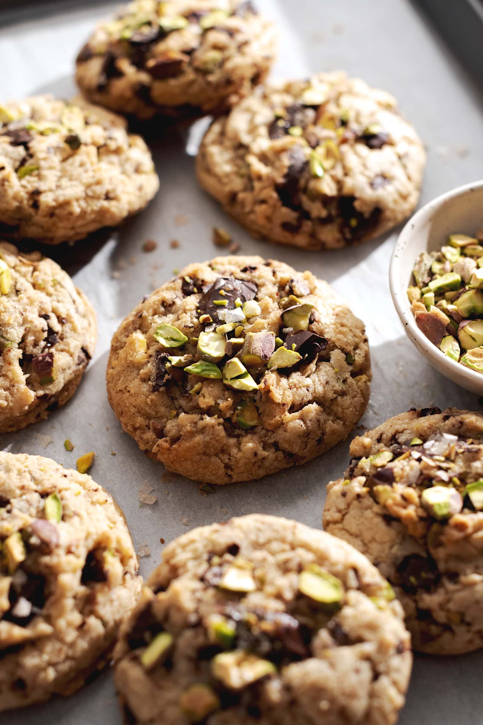 Pistachio chocolate chip cookie surrounded by many other cookies on a baking tray.
