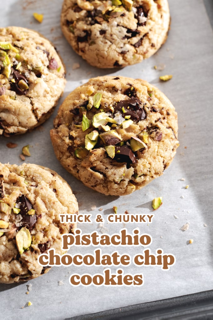 Four chocolate chip cookies with pistachios on top on parchment paper.