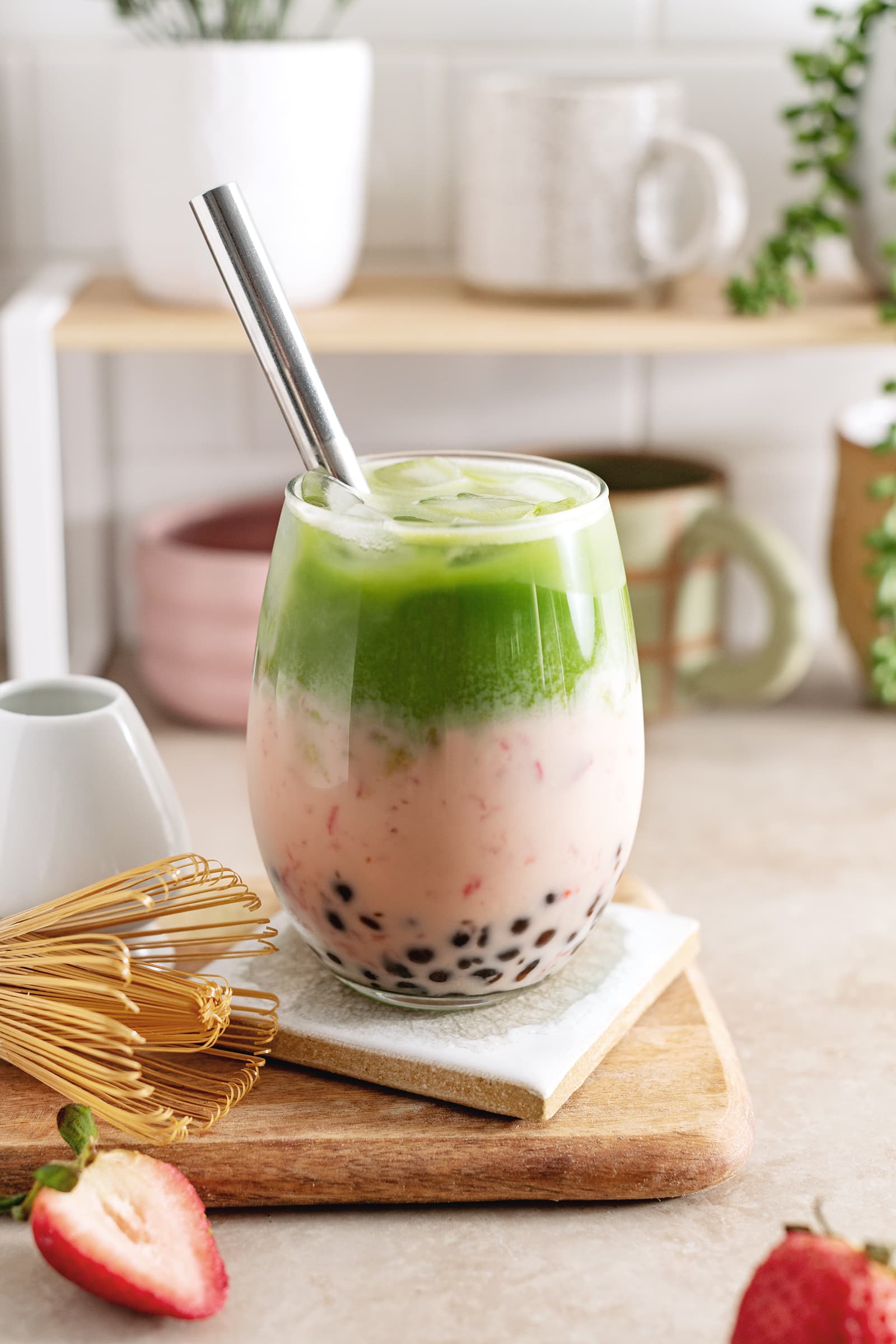 Strawberry matcha boba in a glass with straw and matcha whisk on the side.