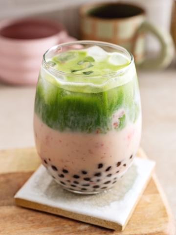 Glass filled with boba pearls, strawberry milk, and matcha split into two layers.