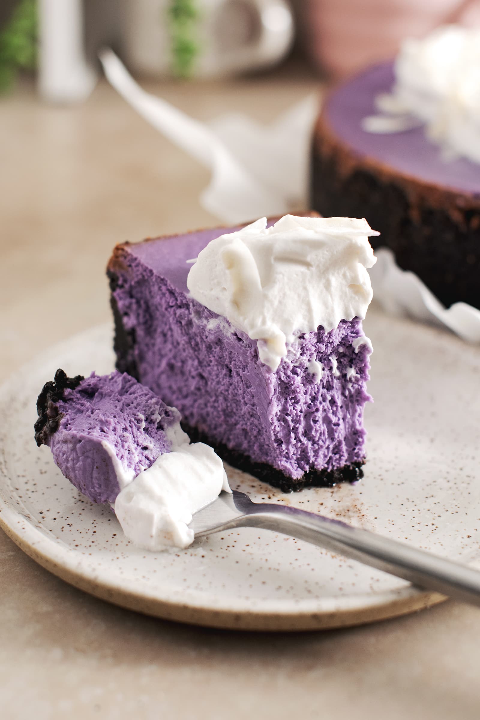 A slice of ube cheesecake with a forkful of cheesecake laying next to it.