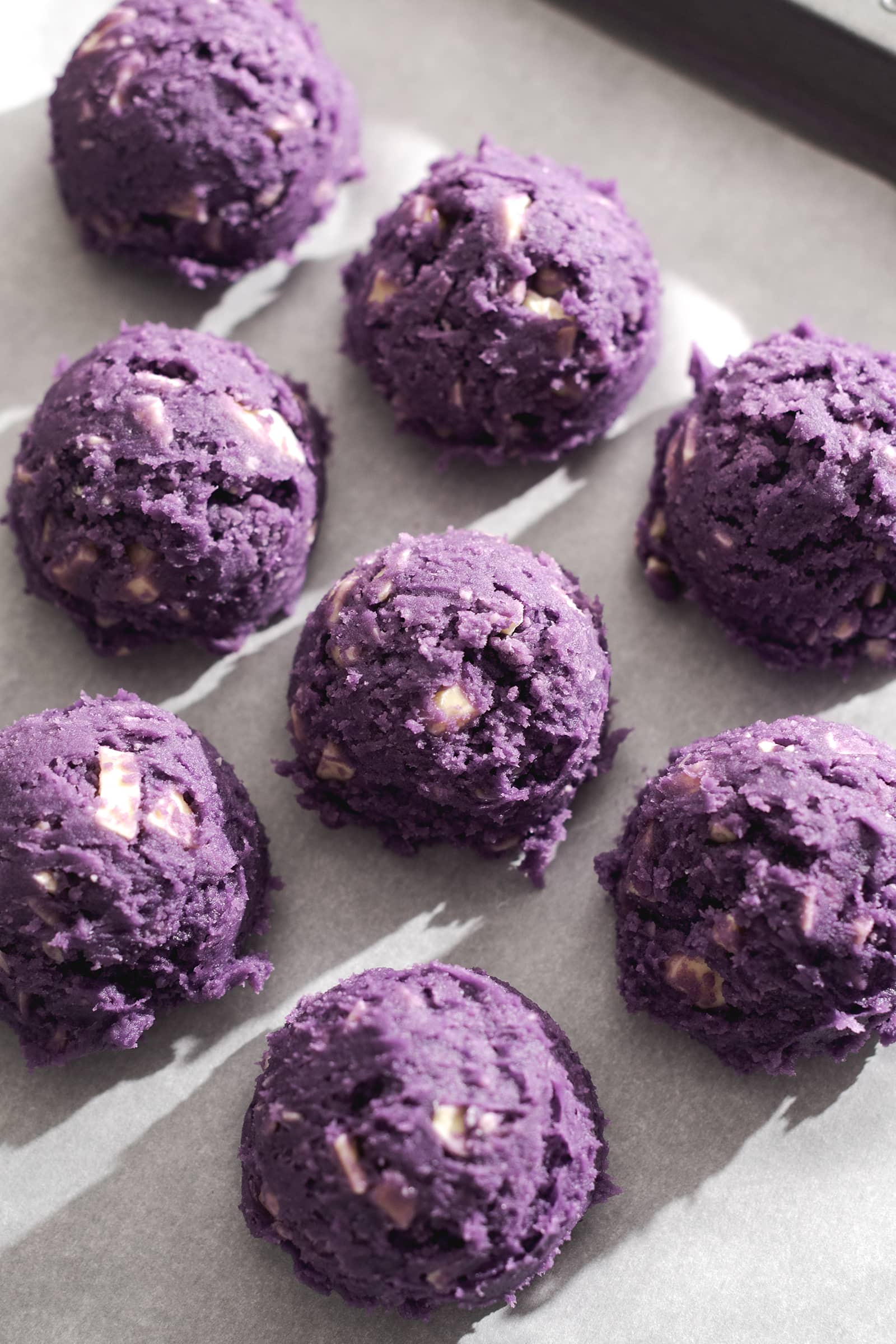 Balls of purple cookie dough lined up on a baking sheet.