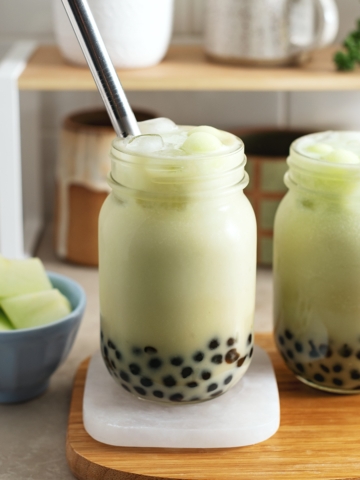 Two glasses of honeydew bubble tea on a wooden platter.