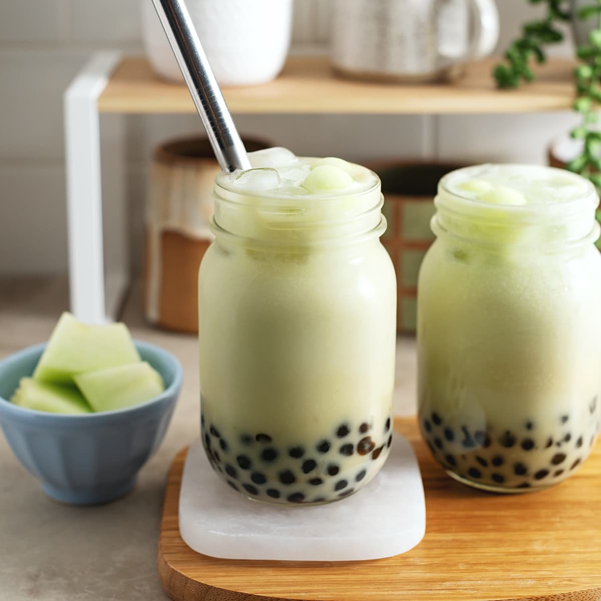 Two glasses of honeydew bubble tea on a wooden platter.