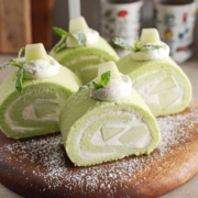 Four slices of honeydew roll cake sprinkled with powdered sugar on a wooden platter.