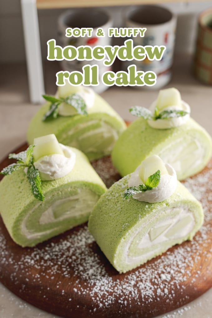 Four slices of honeydew roll cake sprinkled with powdered sugar on a wooden platter.