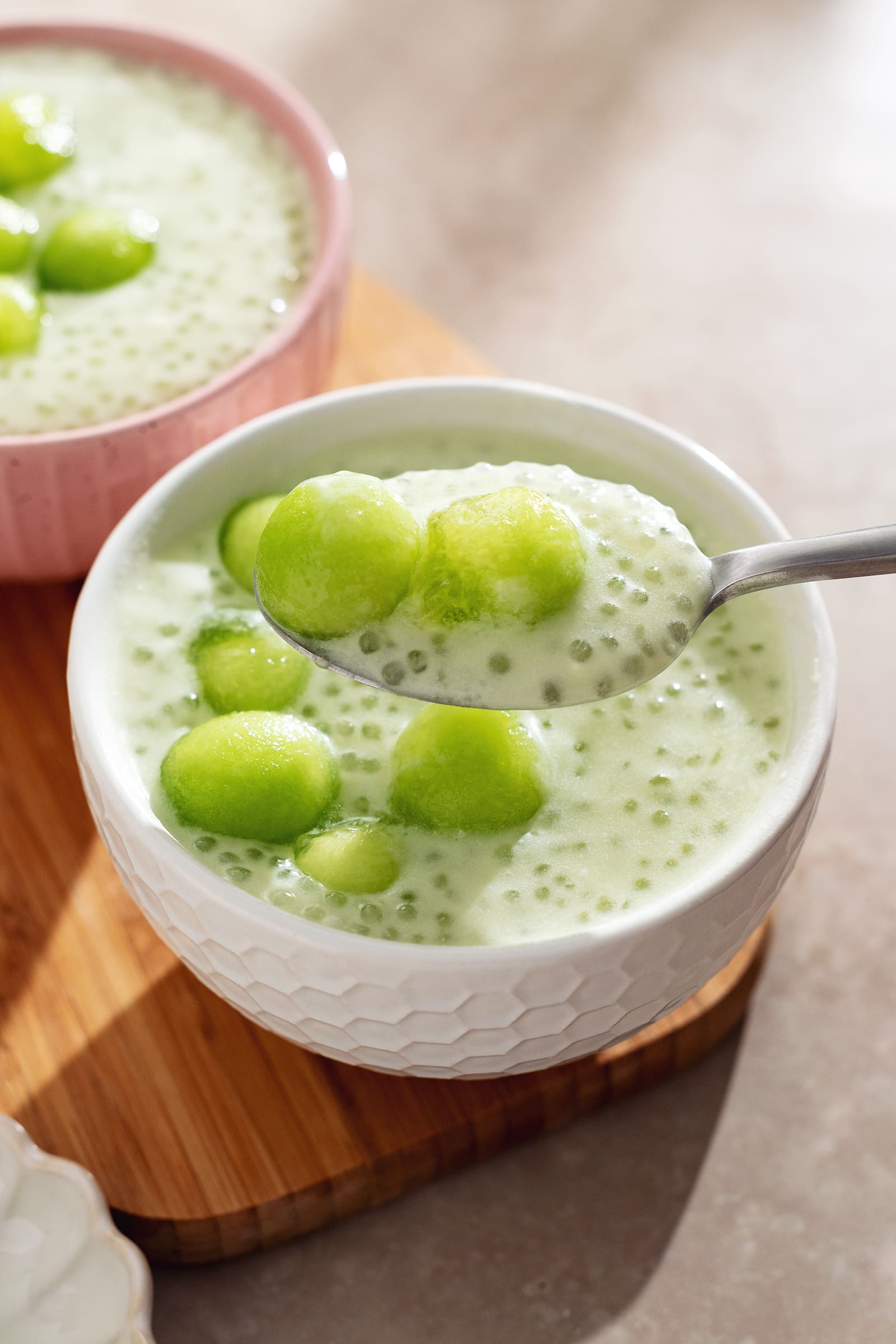 A spoonful of honeydew sago and two melon balls held above a bowl.