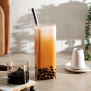 Thai milk tea boba in a rectangular glass with metal straw and small serving containers on either side.