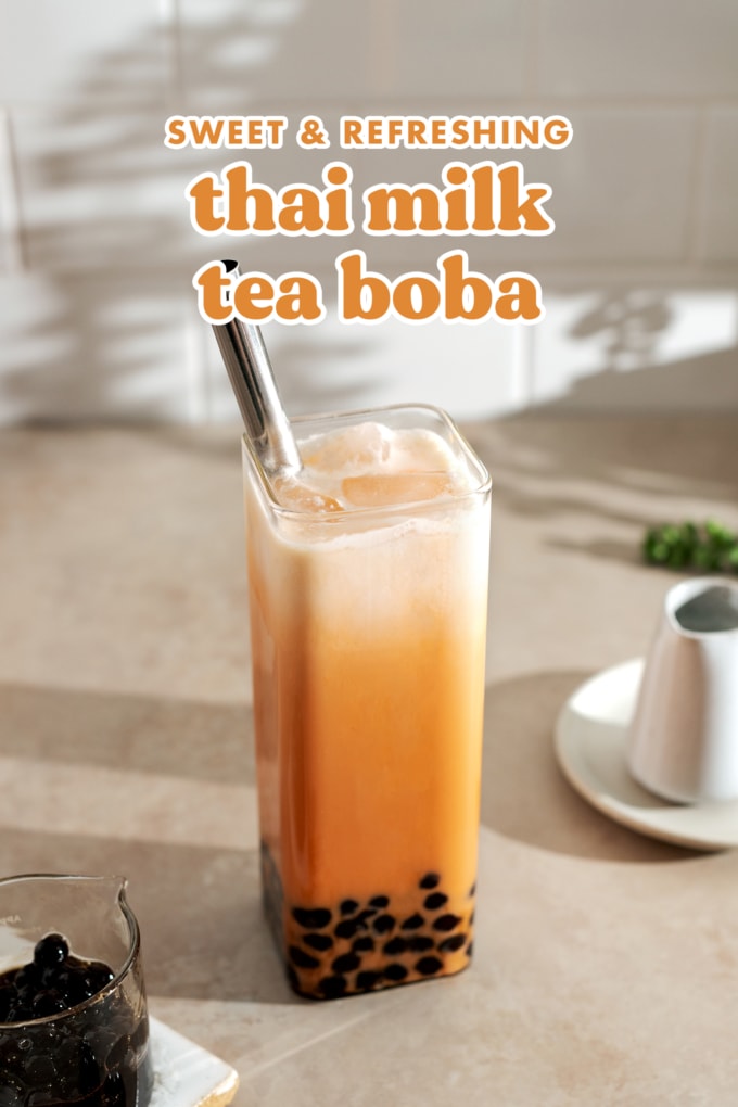A glass of thai milk tea with boba pearls at the bottom and a layer of cream on top with a metal straw.
