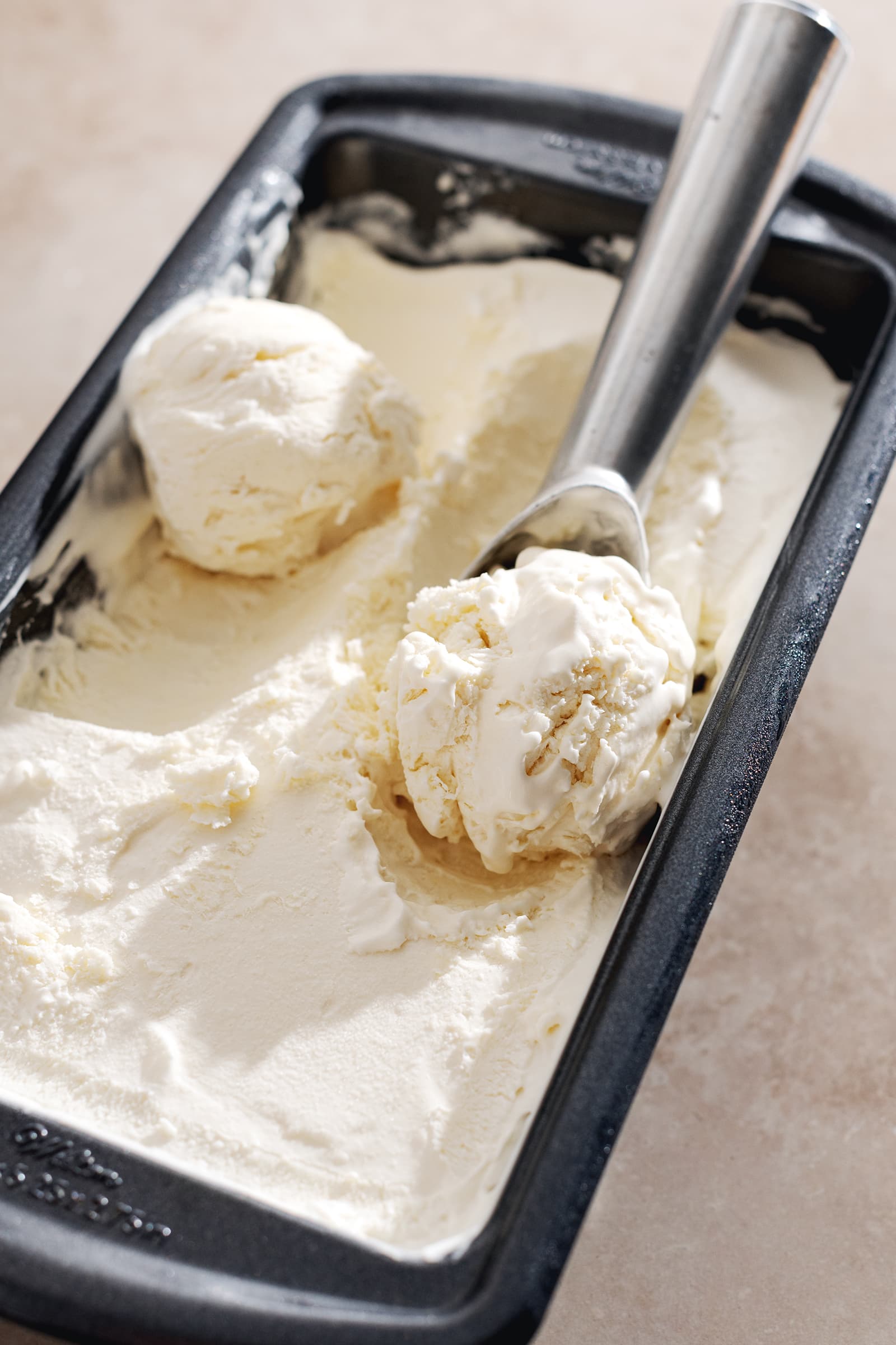 Balls of ice cream in a tin with an ice cream scooper.