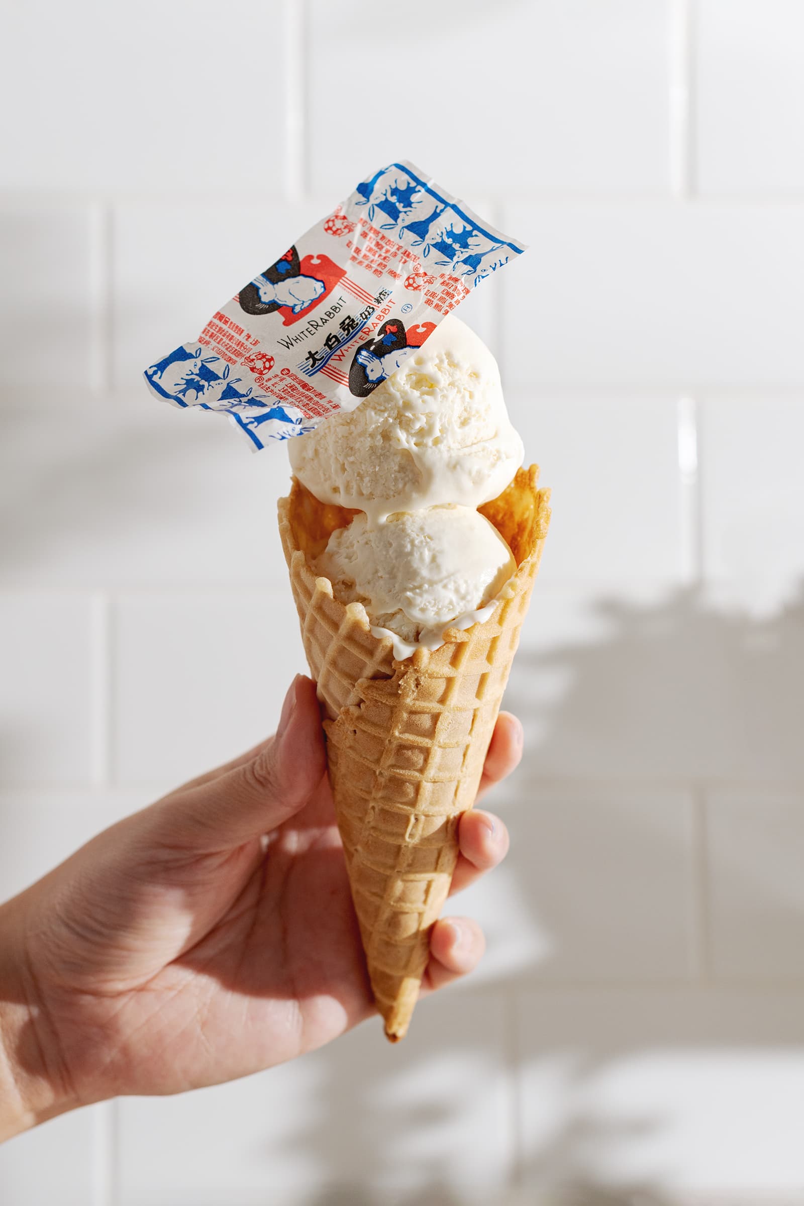 Hand holding an ice cream cone with two scoops of ice cream and white rabbit candy wrapper on top.